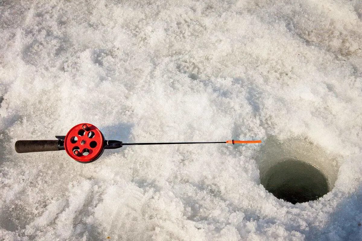 small fishing rod in snow next to a hole in the ice . Ice fishing in Finland - Things to do in winter in Europe