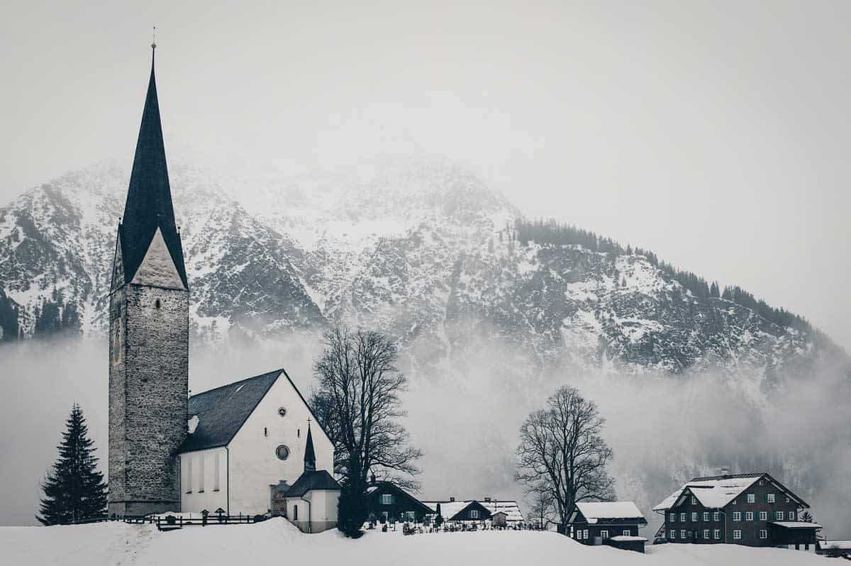Church with tall spire in Europe in winter surrounded with snow. 