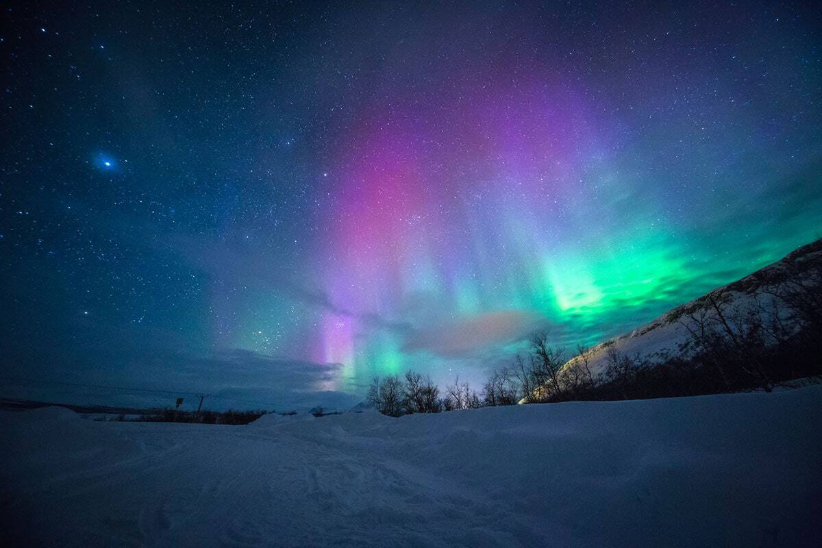 Pink and green northern lights over a snow scape - Seeing the northern lights is one of the best things to do in Europe in the winter