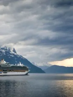 Cruise ship steaming through a wintery fjord with snow capped mountains in the background. These are some of the best winter cruises.