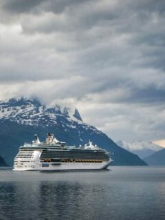 Cruise ship steaming through a wintery fjord with snow capped mountains in the background. These are some of the best winter cruises.