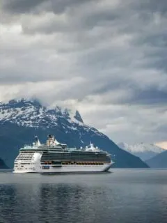 Cruise ship steaming through a wintery fjord with snow capped mountains in the background. These are some of the best winter cruises.
