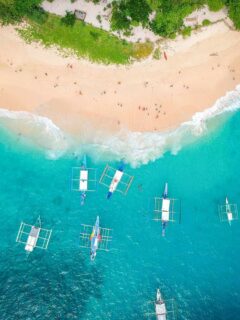 An aerial view of boats anchored in clear water off a white sand beach. Just one of the idyllic scenes from the best places to visit in Southeast Asia