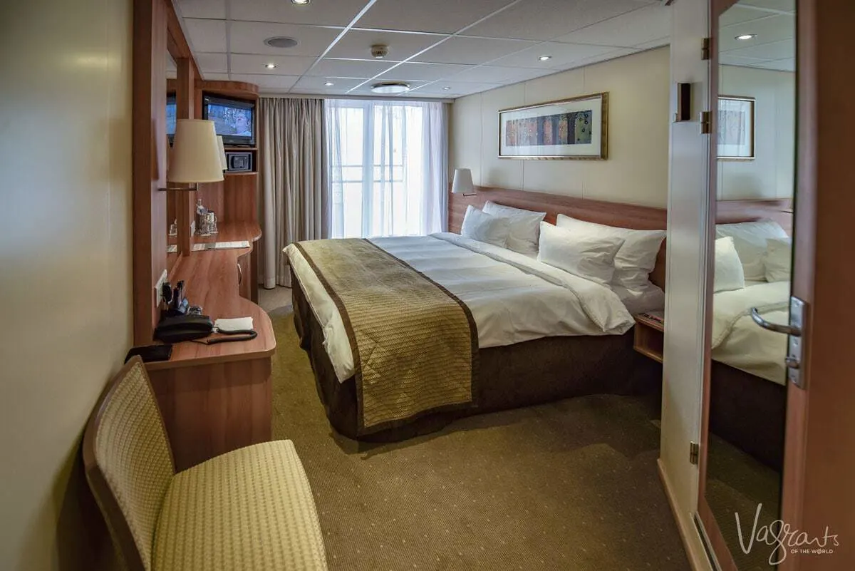 A stateroom on a Viking river cruise showin the bed, window and dresser. Wondering what to pack for a cruise? Remember there is limited space inside these cabins and you want your bulky luggage to fit under the bed.