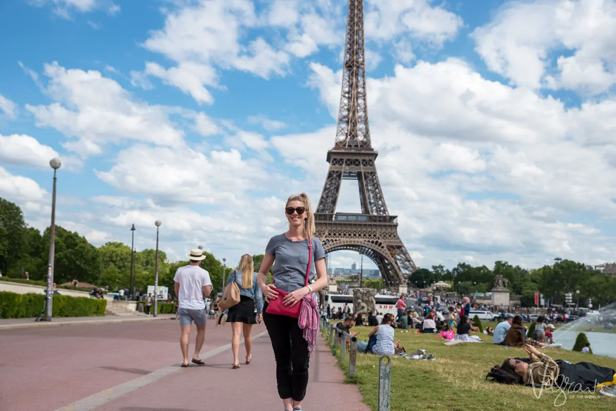 Young girl standing in front of the Eiffel Tower in Paris wearing a crossbody handbag. This is the best type of anti theft purse for travel