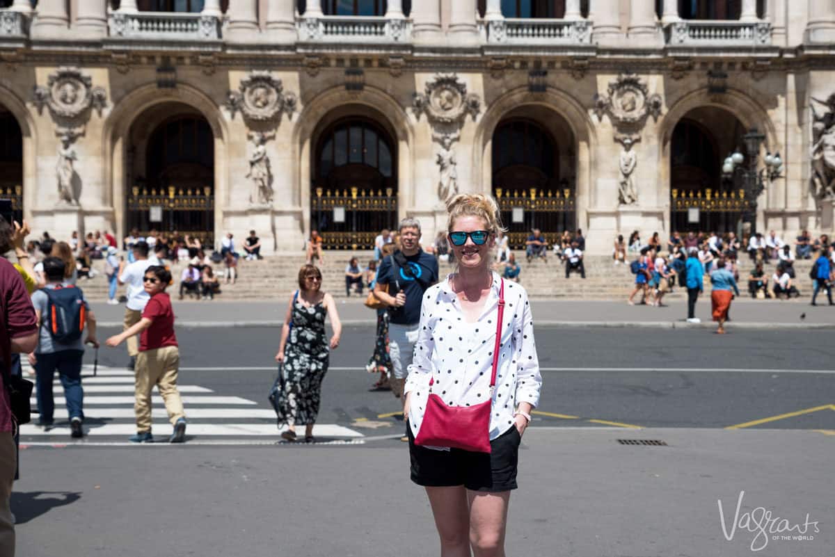 Young girl stading in a busy street in Paris wearing a pink crossbody purse. A good anti theft crossbody hand bag is the best travel purse. 