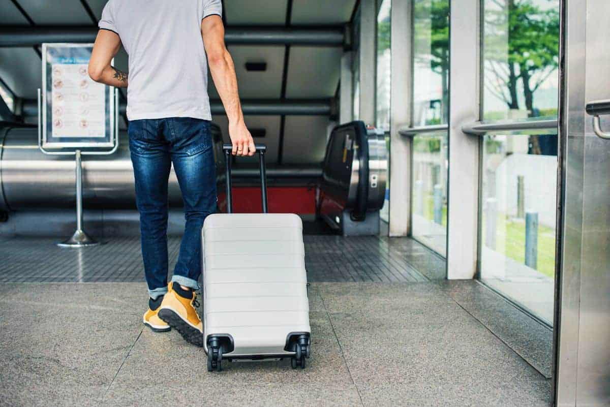 Man pulling suitcase through an airport. Make sure you have the best travel locks for all your luggage when you travel. 