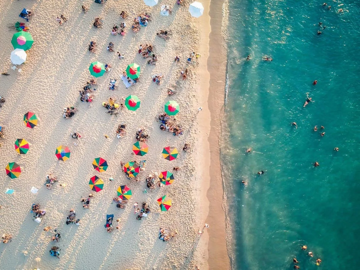 Beach and blue ocean with colourful umbrellas and beach goers. 