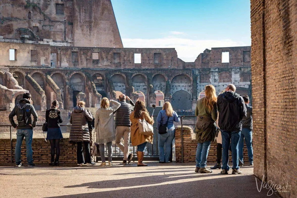 A group of tourists standing in the sun looking into the Colosseum in Rome.