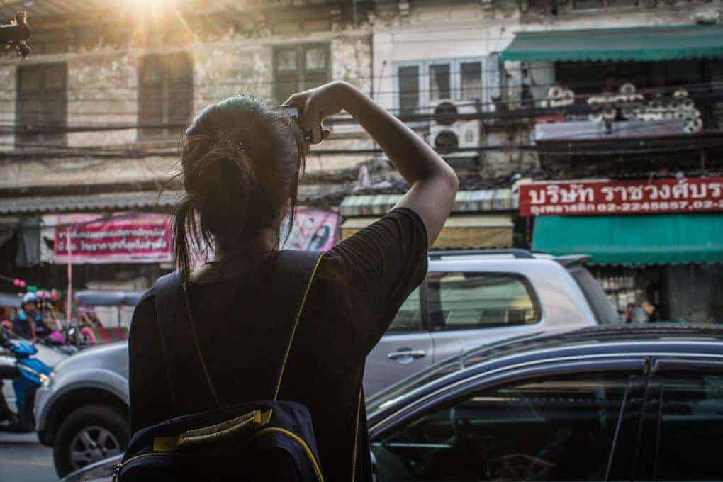 Girl with backpack taking a photo of a street scene in Asia. Notifying your bank of your travel plans id=s a great safe travel tip, especially when travelling in Asia