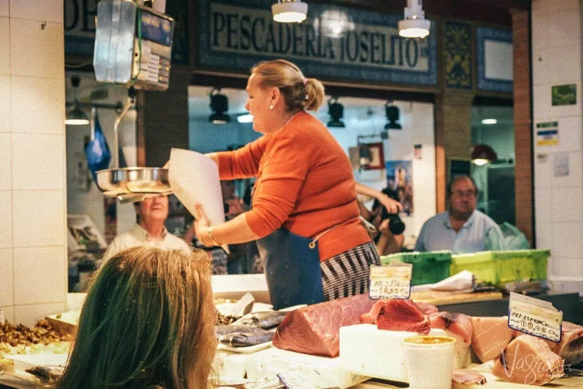 Woman in orange weighing fish at the Triana Market. 