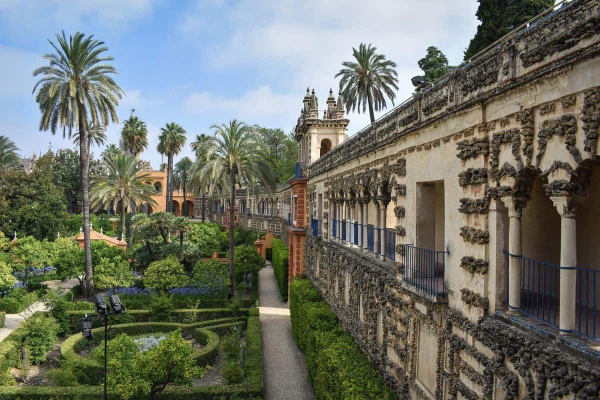 The gardens with palm trees and manicured shrubs next to the wall of Royal Alcazar, One of the most popular attractions in Seville.