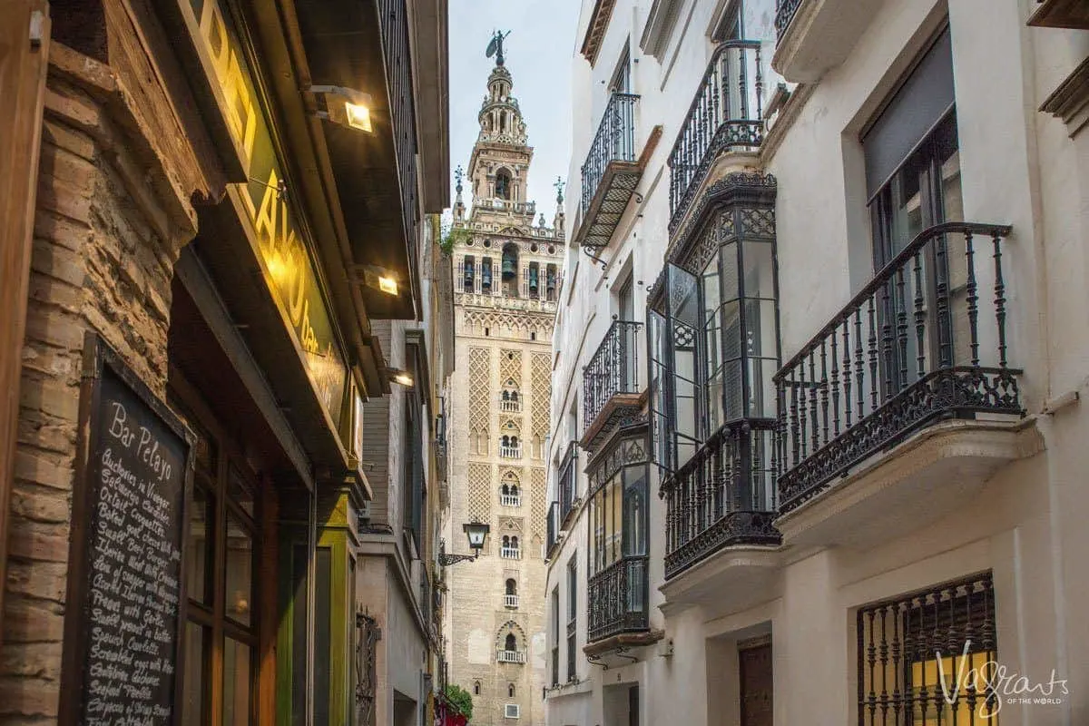 The Giralda Tower viewed from down a narrow street lined with balconies. 