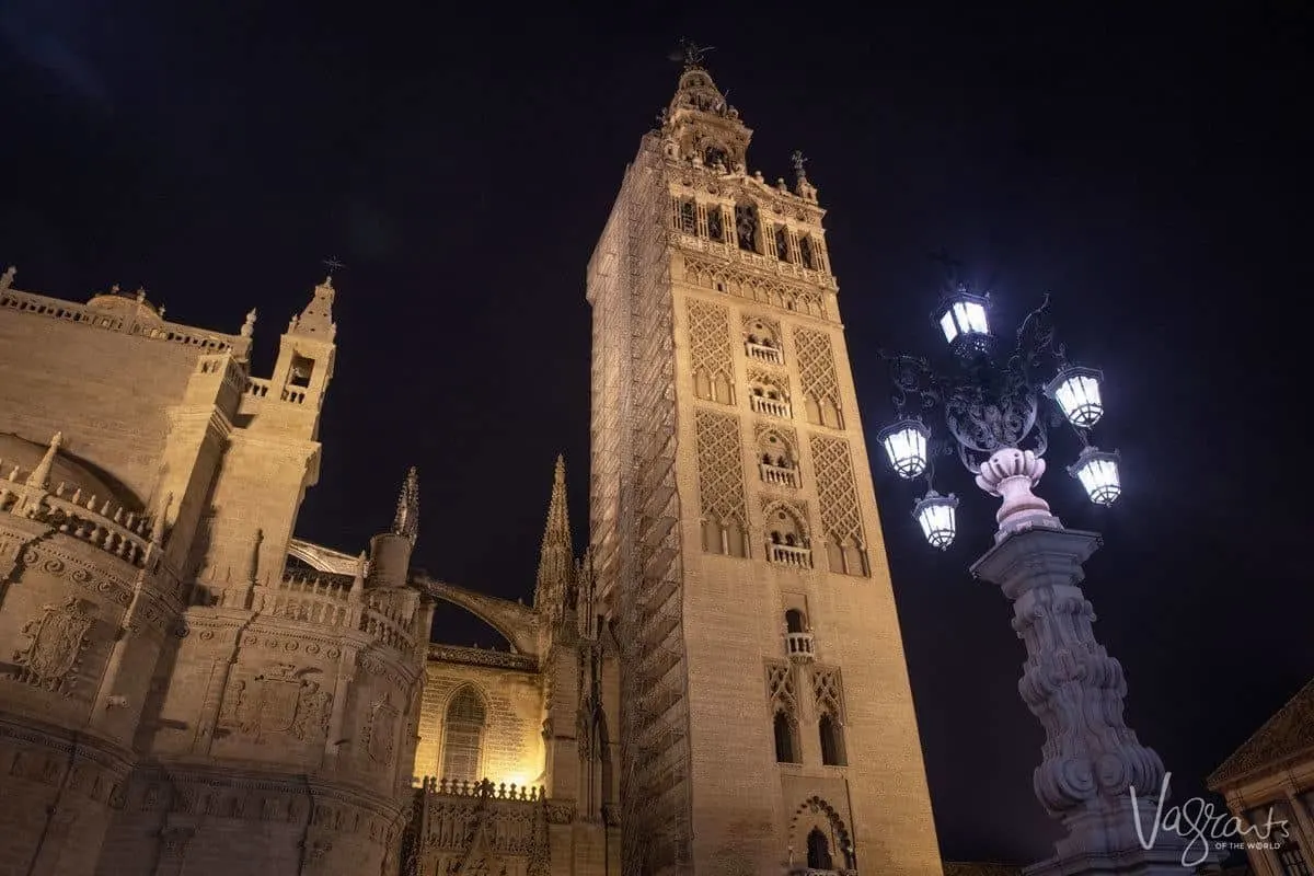 The Giralda Tower with an ornate street lamp in front at night in Seville Spain.