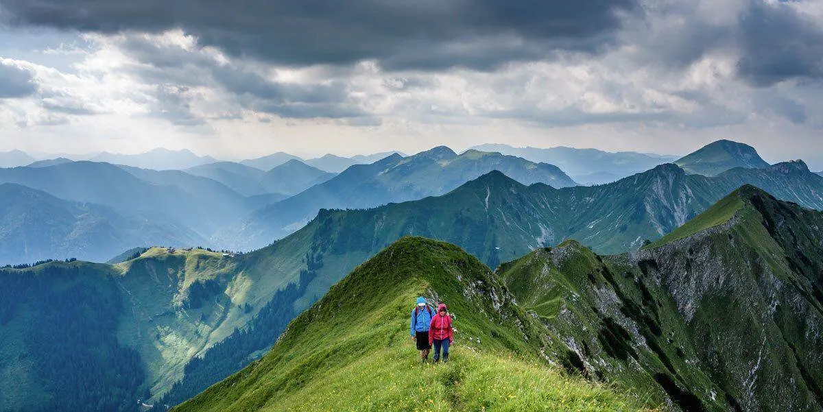 two walkers on a grassy ridge at high altitude.