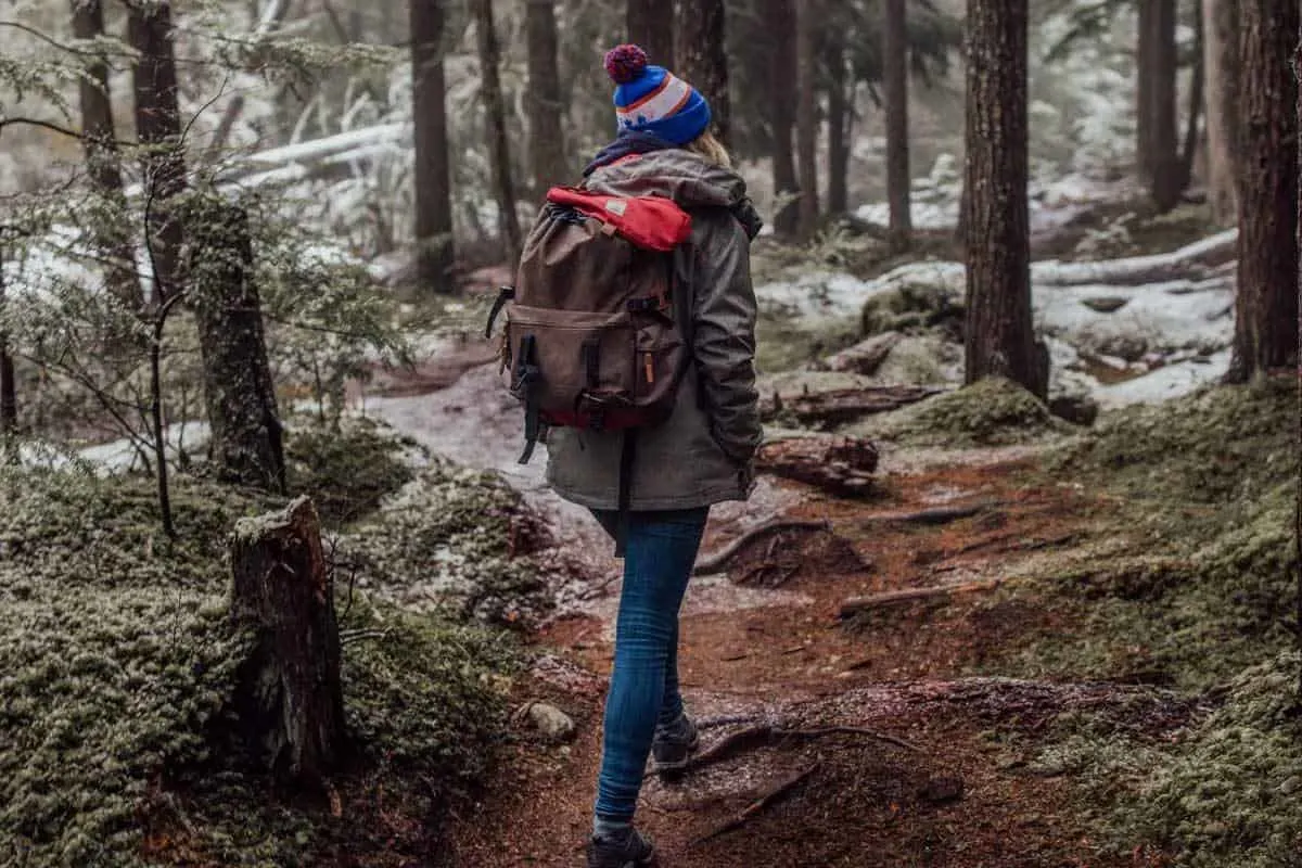 Hiker in beanie and backpack walking through frosty forest. 