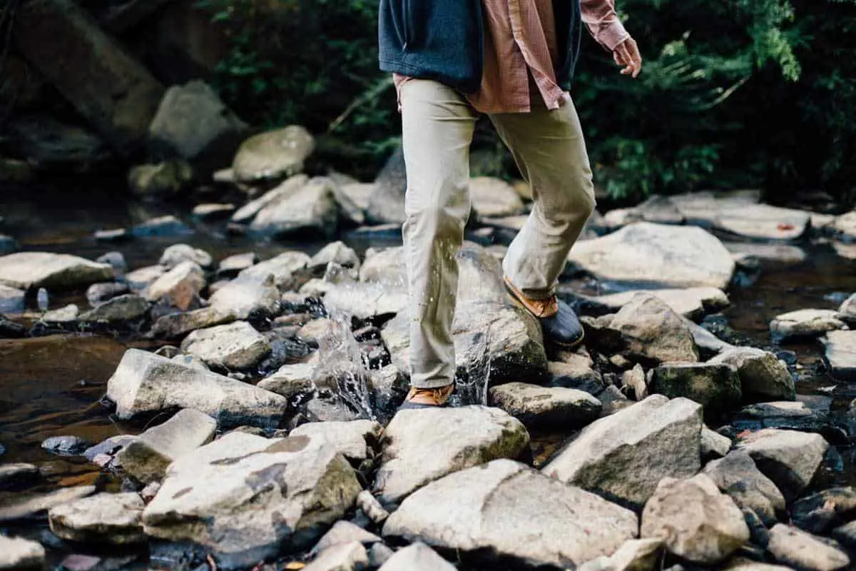 Man in hiking boots and quick dry pants walking on rocks to cross a stream. 