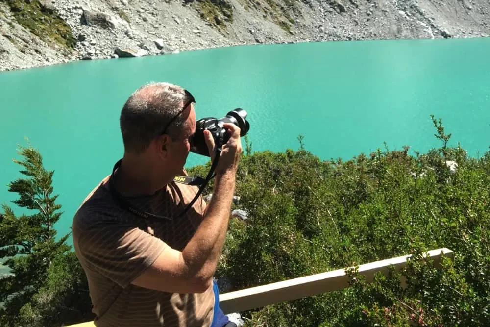 Man holding camera taking a shot across a lake. 