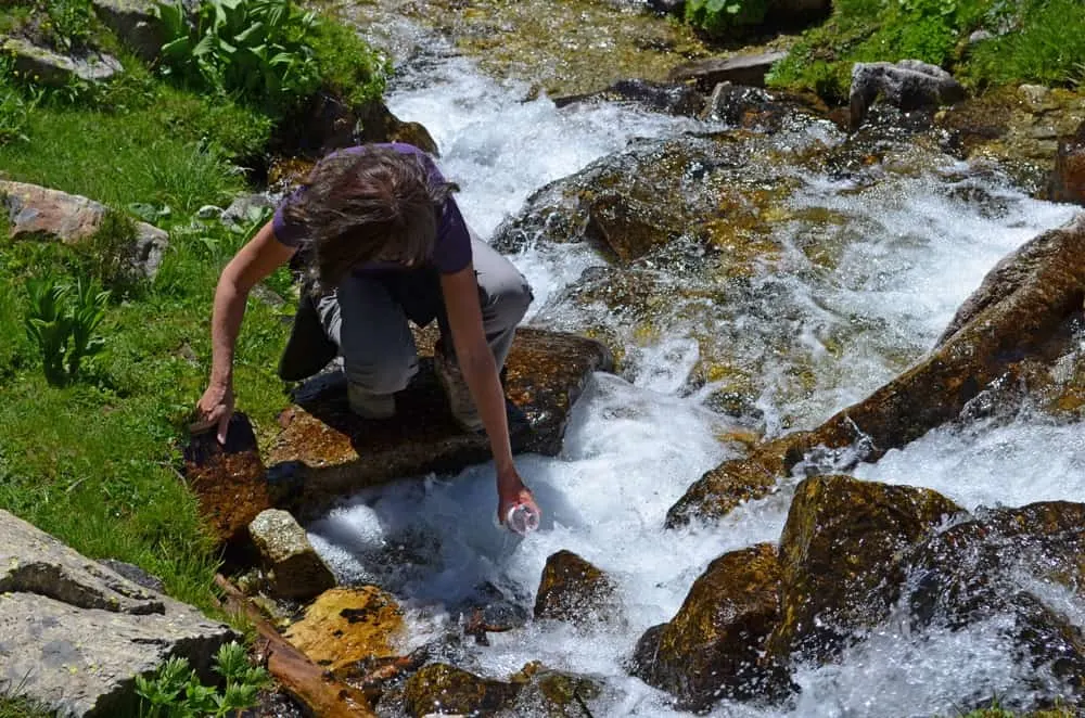 Walker filling water bottle from a flowing stream. 
