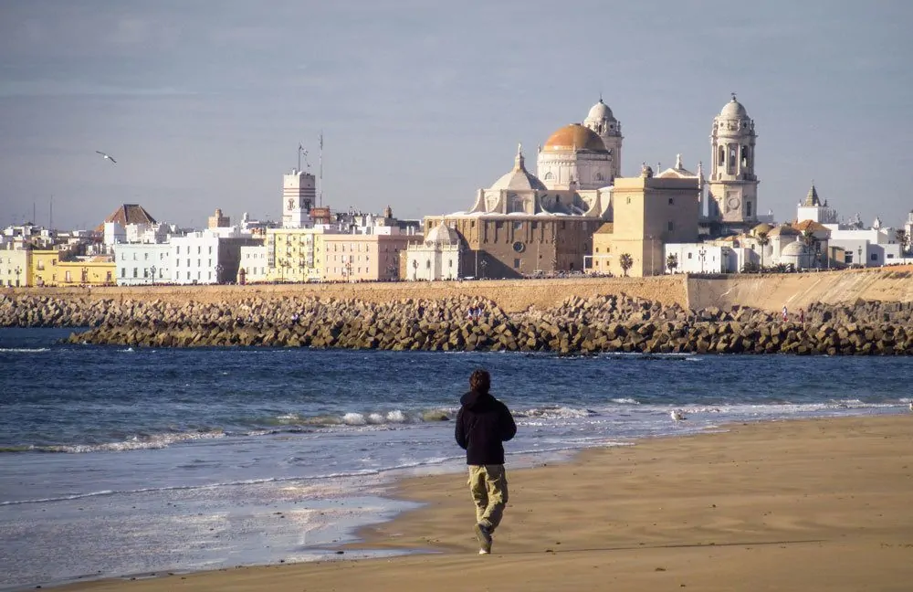 man walking on the beach in Cadiz. Looking for free things to do in Cadiz, the beach is a great choice. Add this to your Seville itinerary and do a Day trip from Seville to Cadiz