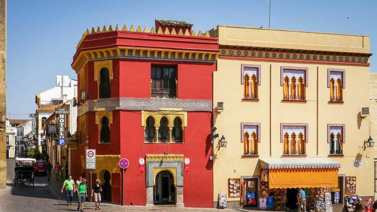 Colourful red and yellow street corner with tourists wandering past. Add Cordoba to your best Day trips from Seville itinerary