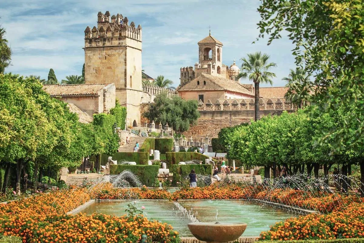 Terrace gardens with colourful flowers and castle in the background. One of the best things to do in Cordoba is to visit this area. Day trips from Seville to Cordoba