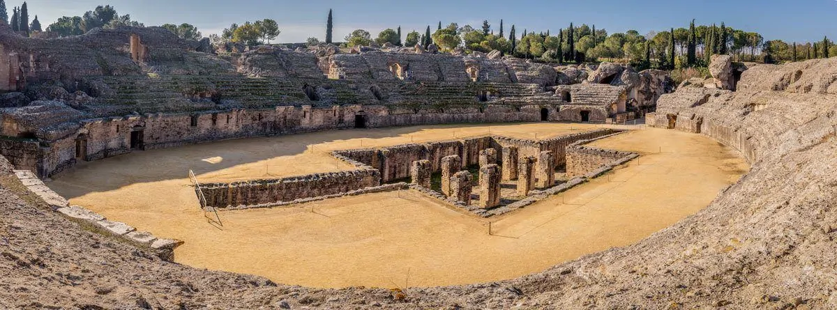  Italica Roman Ruins with stone pillars inside a sandy arena. This is one of the Best Day Trips from Seville