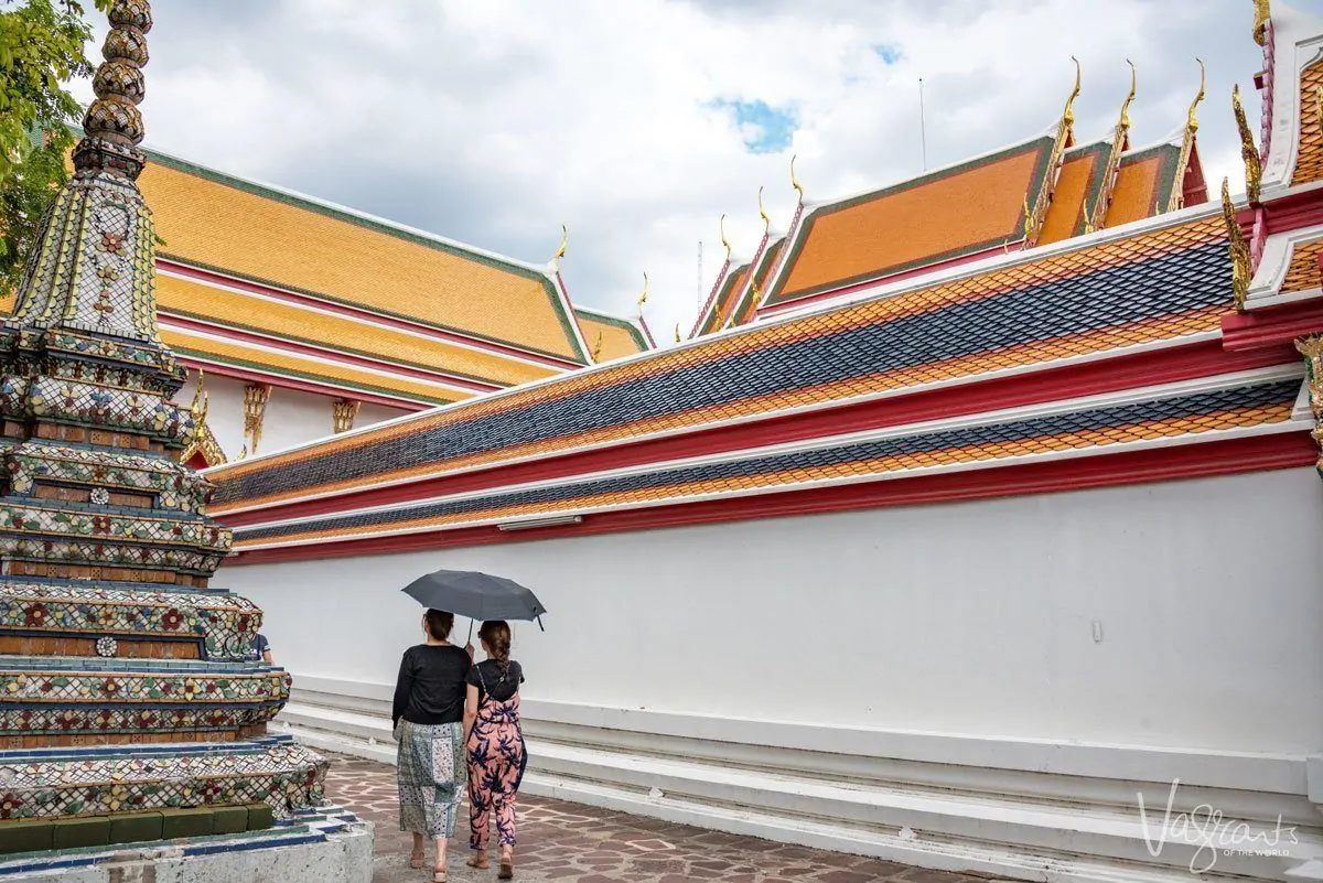 two women walking around a multicoloured shrine in bangkok. having people in your shot will help with getting the best travel photographs