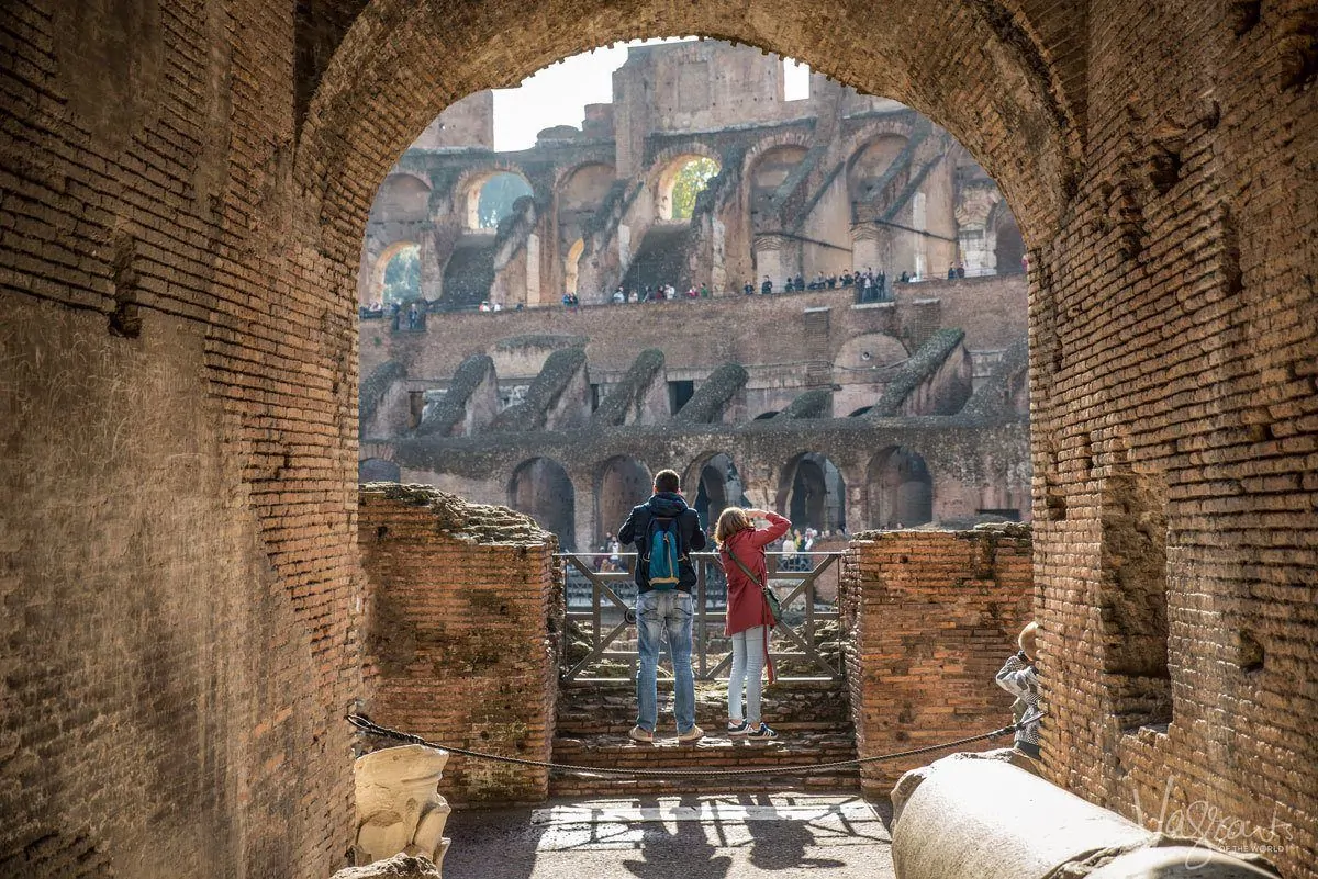 two people in an archway overlooking the colosseum in rome taking photographs. getting the right composition is very important when you want to get the best travel photos.