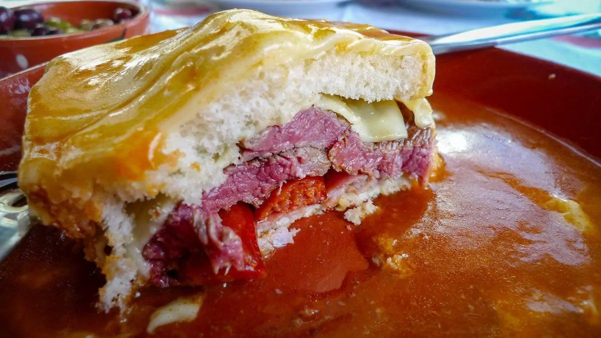 A typical francesinha sandwich, a cheese covered meat sandwich floating in tomato beer sauce.