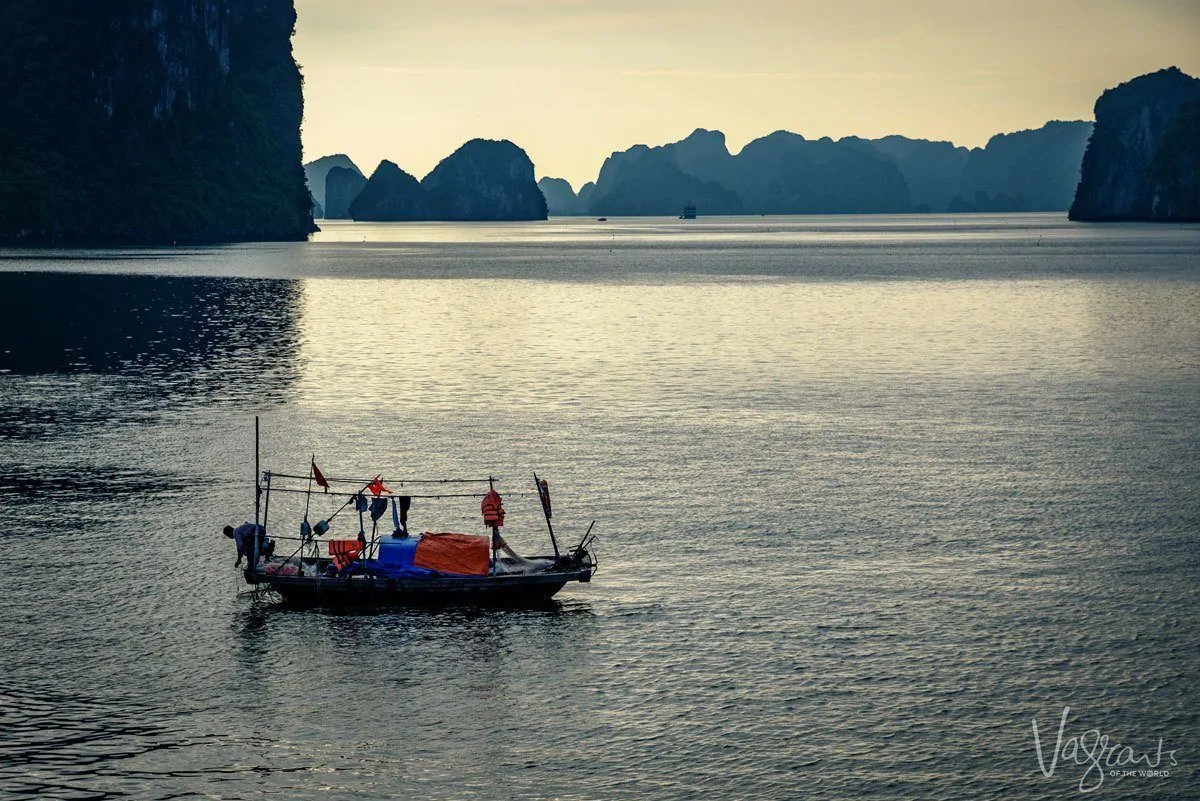 a junk floating across halong bay with large rock formations erupting from the water in the background. Sometimes just being in the right place and knowing it is a landmark and travel photography tip