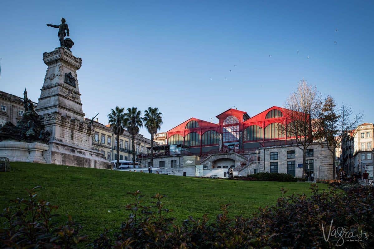 The green grass park with statue in front of the red steel market building. 