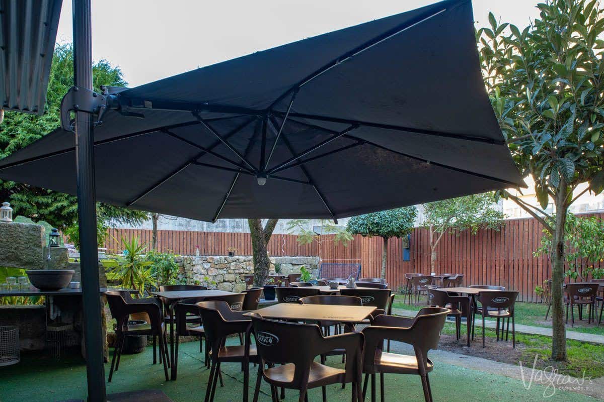 Tables and chairs under a large umbrella in the hidden garden of Shop O Pretinho do Japao. 