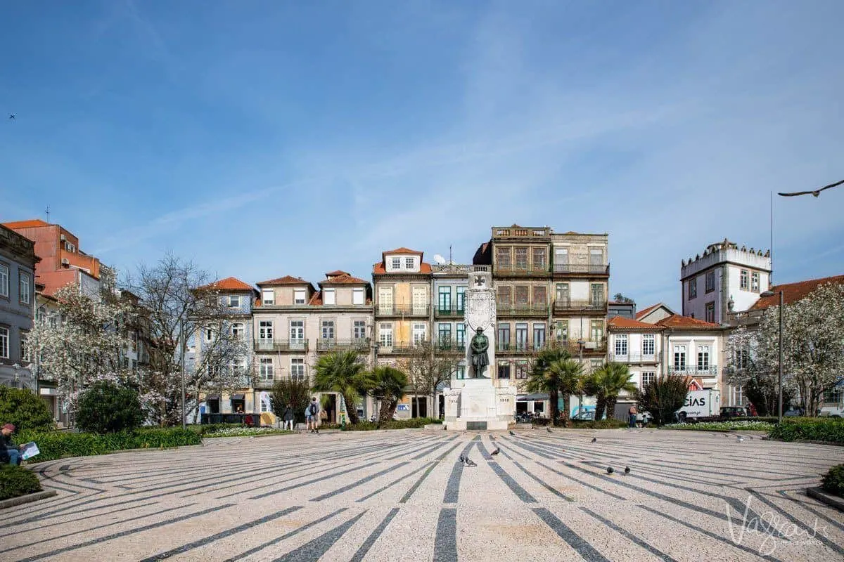 Cobblestoned park with central statue surrounded by colourful houses in the centre of Porto. 