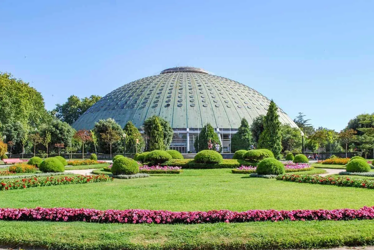 The green grass and flower beds in front of a building that looks like a flying saucer in the Porto Jardins do Palacio de Cristal.