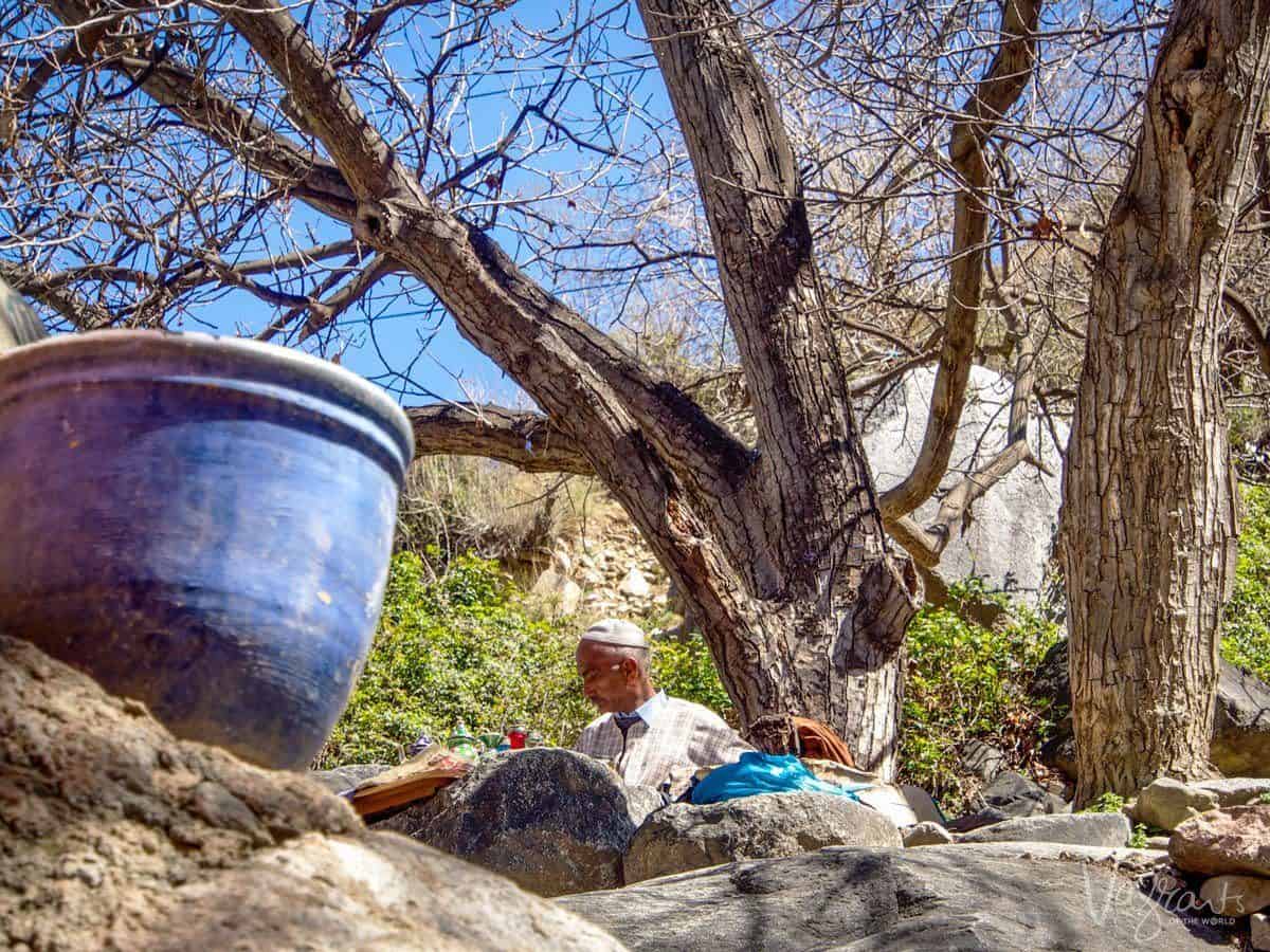 Vendor tending his wares behind a rocky outcrop and large blue pot.