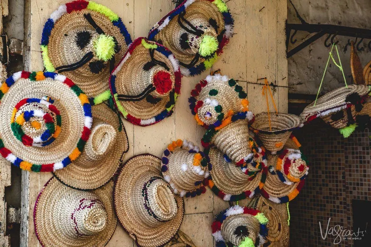 Colourfully embroidered straw hats hanging on a wooden wall for sale in a medina. 