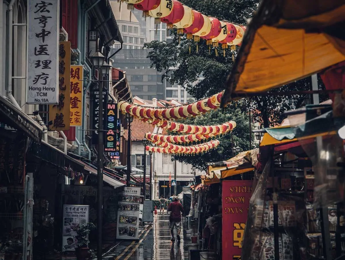 Man walking down street with red and white lanterns overhead. 