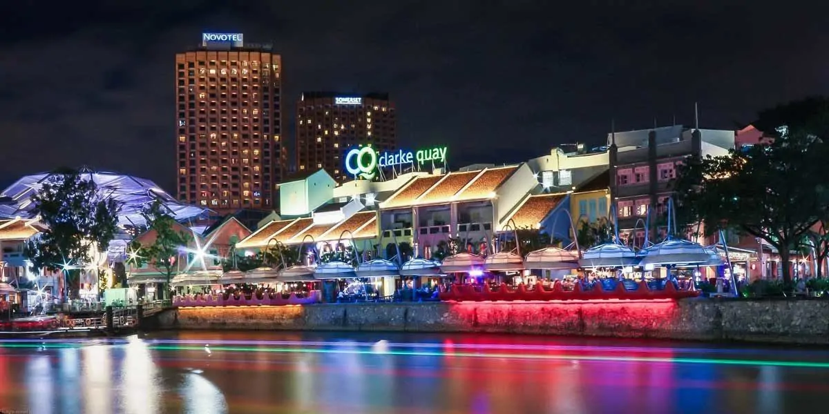 Clarke quay lit in blue red orange with colours reflected on water, a great place for getting cheap drinks.