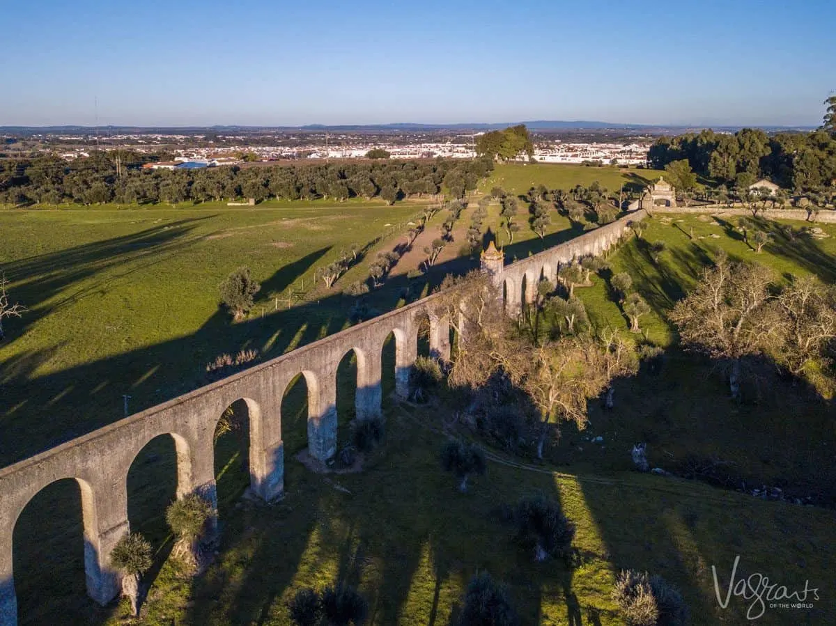 Ancient stone aqueducts dividing a green field, a alentejo highlight.  These can be seen on a day trip from evora or on a alentejo portugal road trip.
