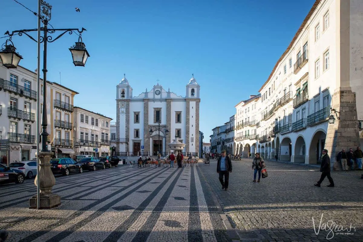 Evora square with mosaic cobblestones and white church.  you can stop here for lunch and a bottle of alentejo wine on your lisbon to evora day trip or at the start of your alentejo road trip.