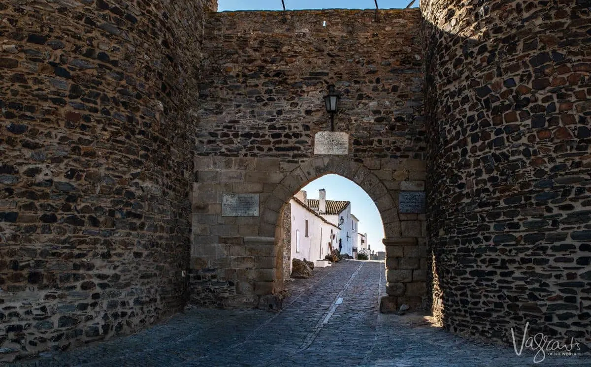archway entrance of Monsaraz castle with cobblestone street leading into the town.  A visit to Monsaraz is one of the best things to do in alentejo portugal