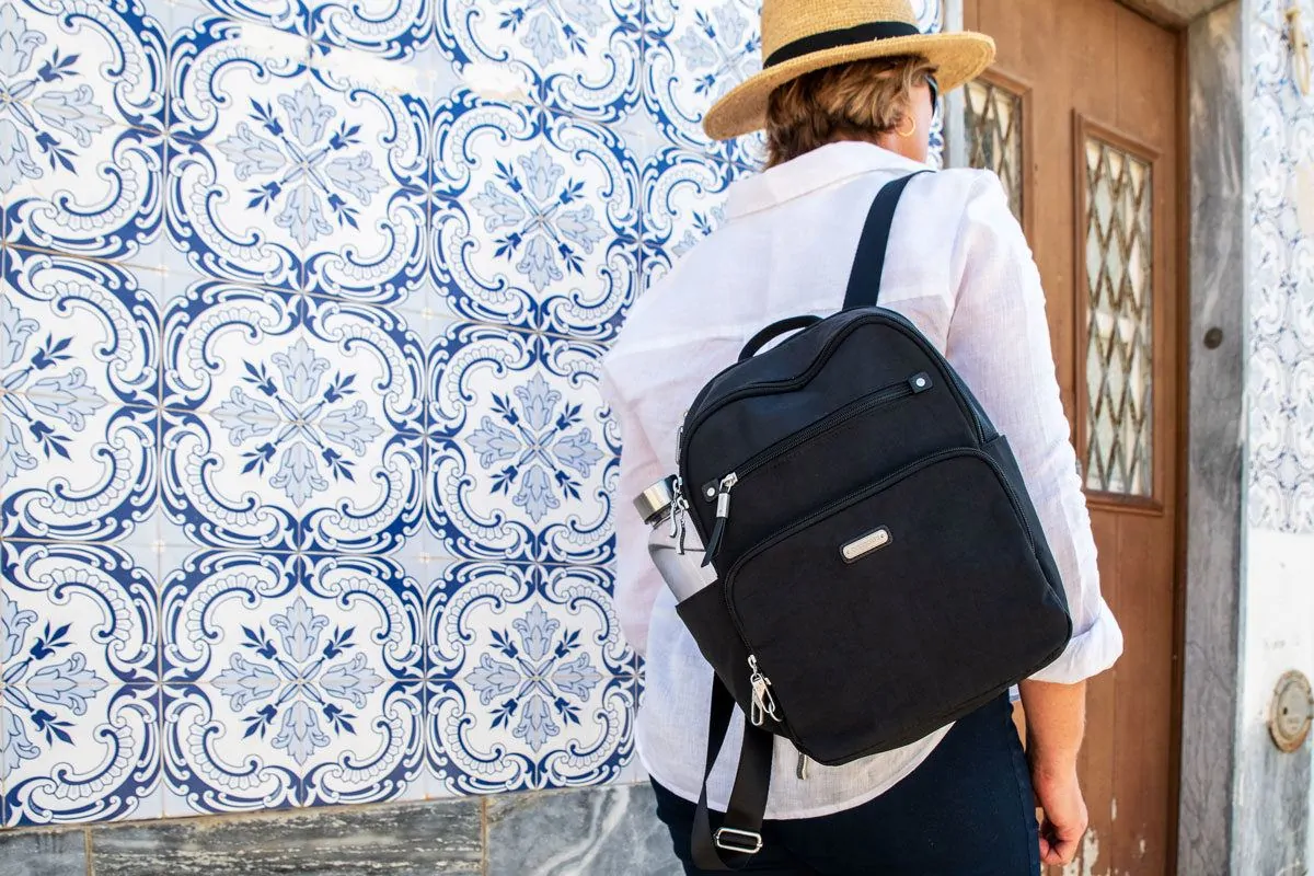 black womens travel backpack slung over the shoulder and set against a blue and white tiled wall.  the may be a womens best travel backpack