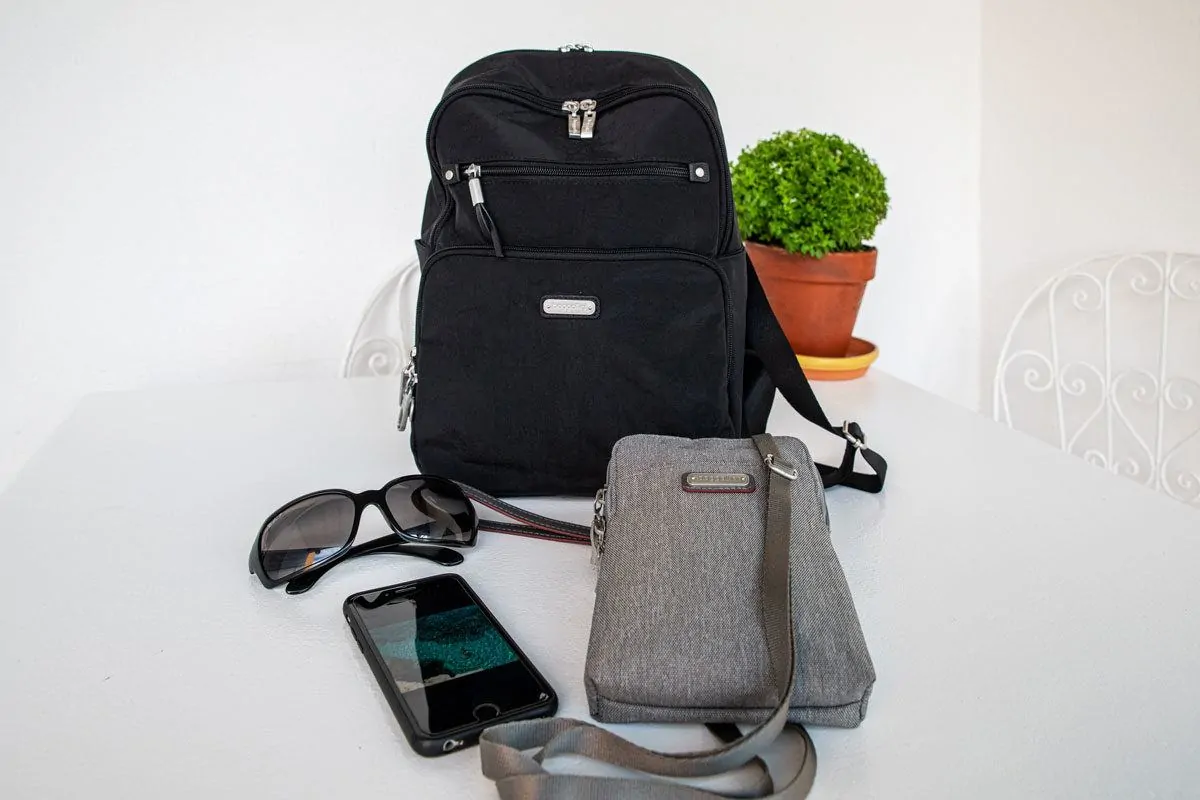 a black cross body bag ad grey travel purse next to sunnies and a phone.  the best travel purses need to have all the features you will find in this article.  that is why baggallini make the perfect womens travel purse