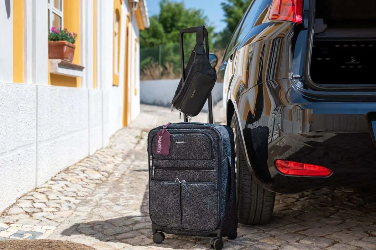 a baggallini carryon travel bag and bum bag sitting next to the open boot of a car.  these bags are the best travel bags for women