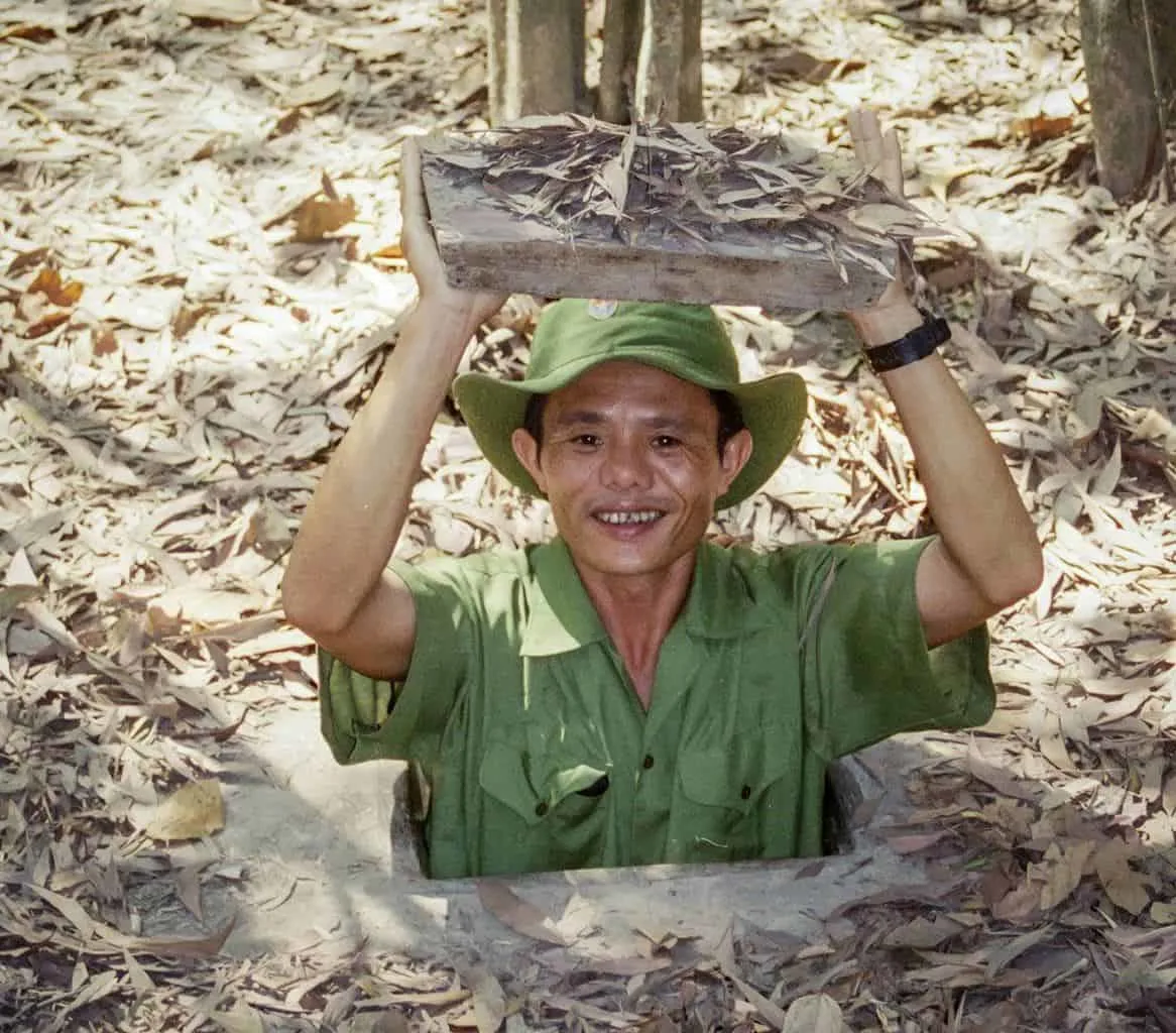 vietnamese man holding lid of tunnel at cu chi tunnels. the best day trip from ho chi minh city