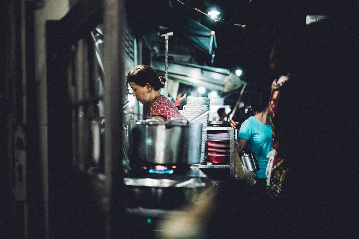 women cooking with pot on the stove in the foreground. The ben thanh markets are a interesting thing to see in Ho Chi Minh city at night.