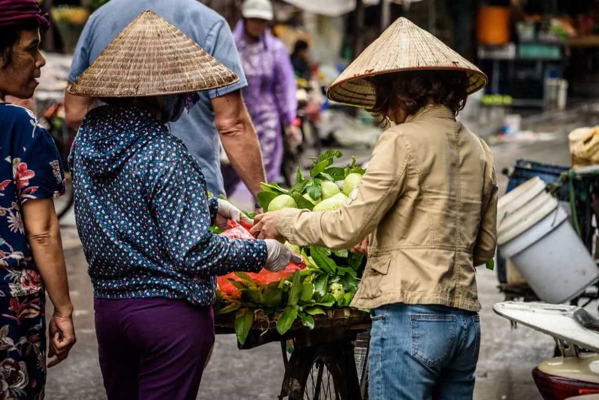 two street vendors wearing conical hats selling vegetables. shopping at the street vendors is a fun thing to do in Ho Chi Minh city