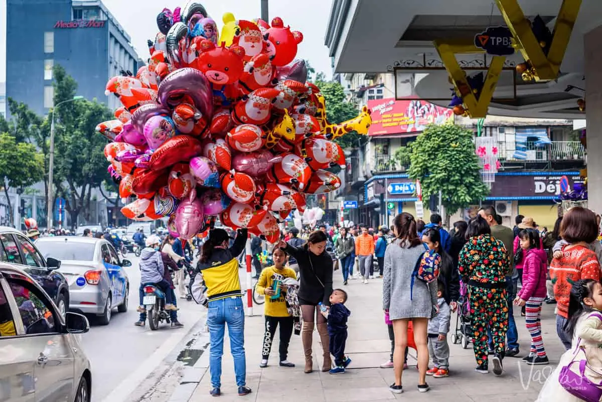 A women holding hundreds of colourful helium balloons on the street. 