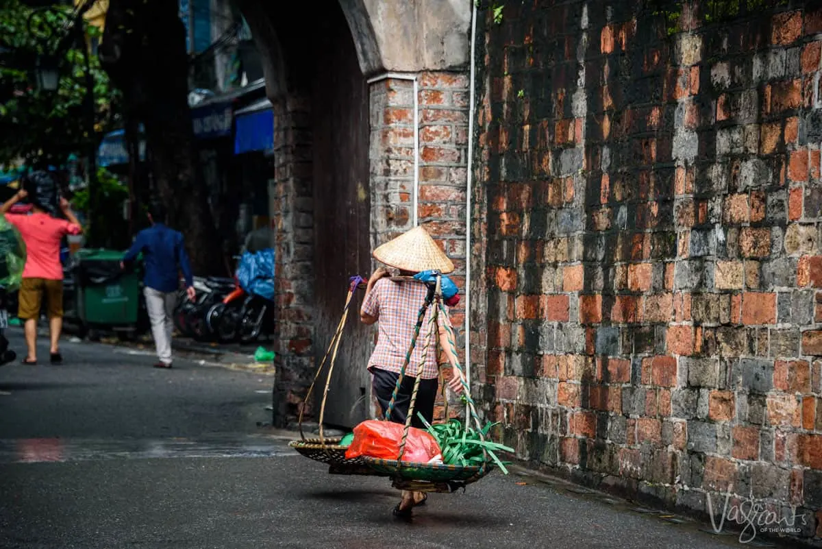 Women in conical hat carrying her vegetables to market. Shopping from these ladies in Hanoi Old Quarter is a great thing to do in Hanoi.